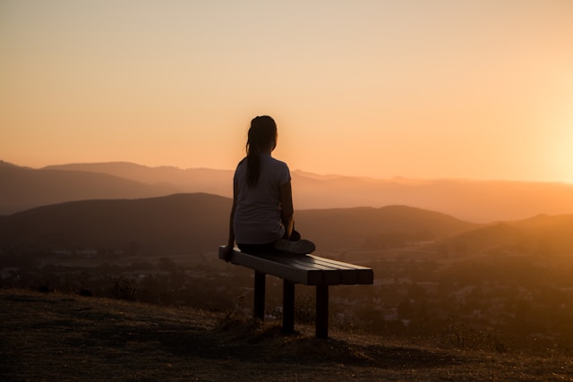 Frau sitzt bei Sonnenaufgang auf einer Bank