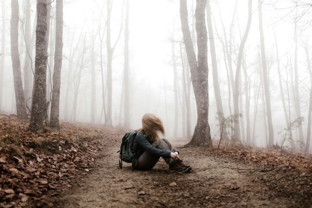 Frau sitzt im nebligen Wald am Boden. Lange Haare im Gesicht.